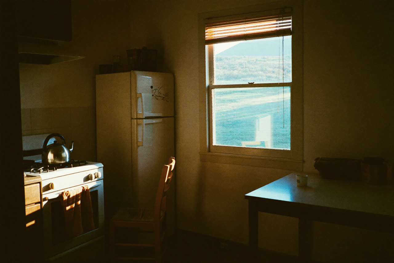 An empty country kitchen at first light, one chair pulled out from the table.