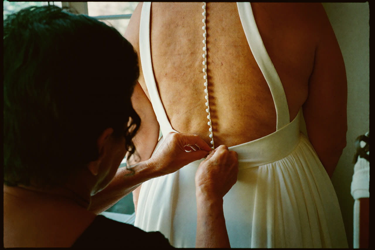 A woman fastening the long row of buttons up the back of a wedding dress.