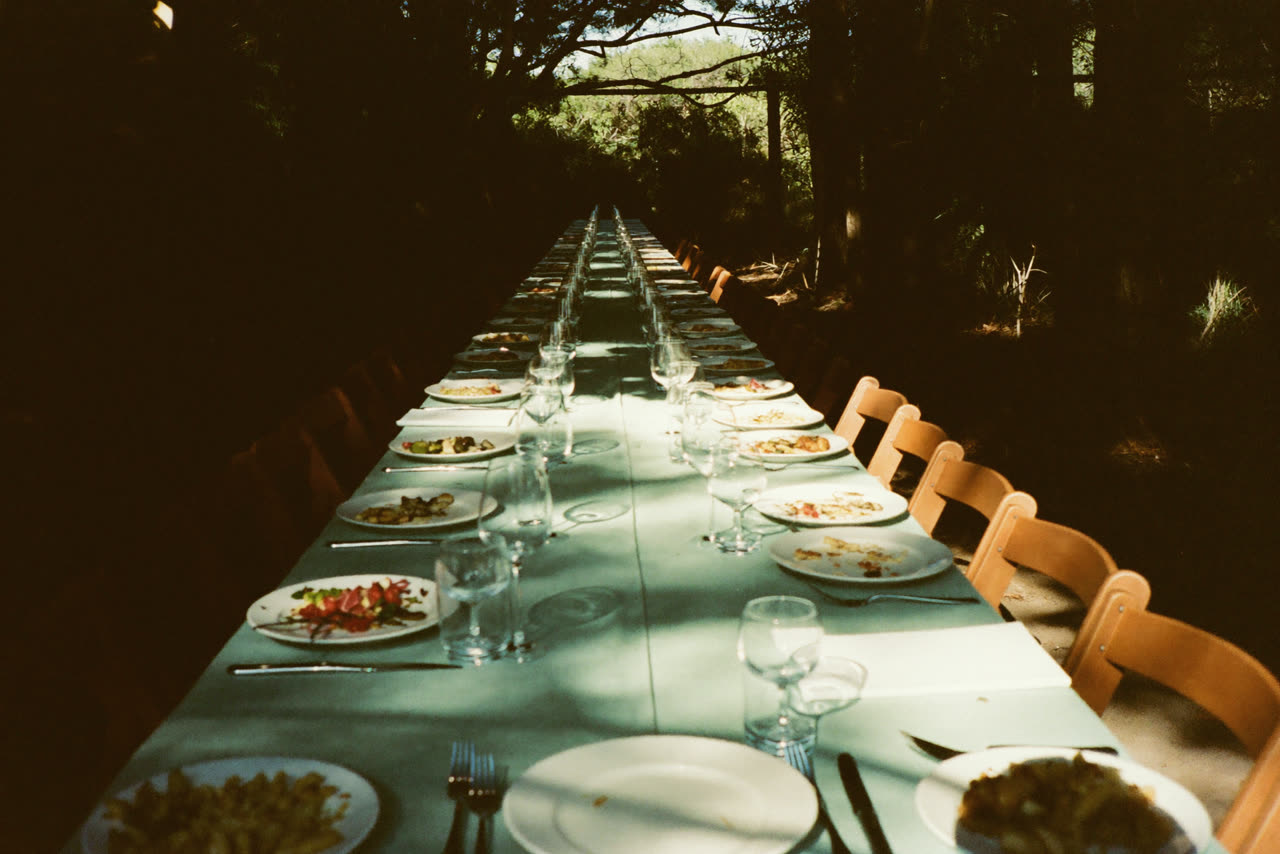 A long outdoor table set for a meal under trees.