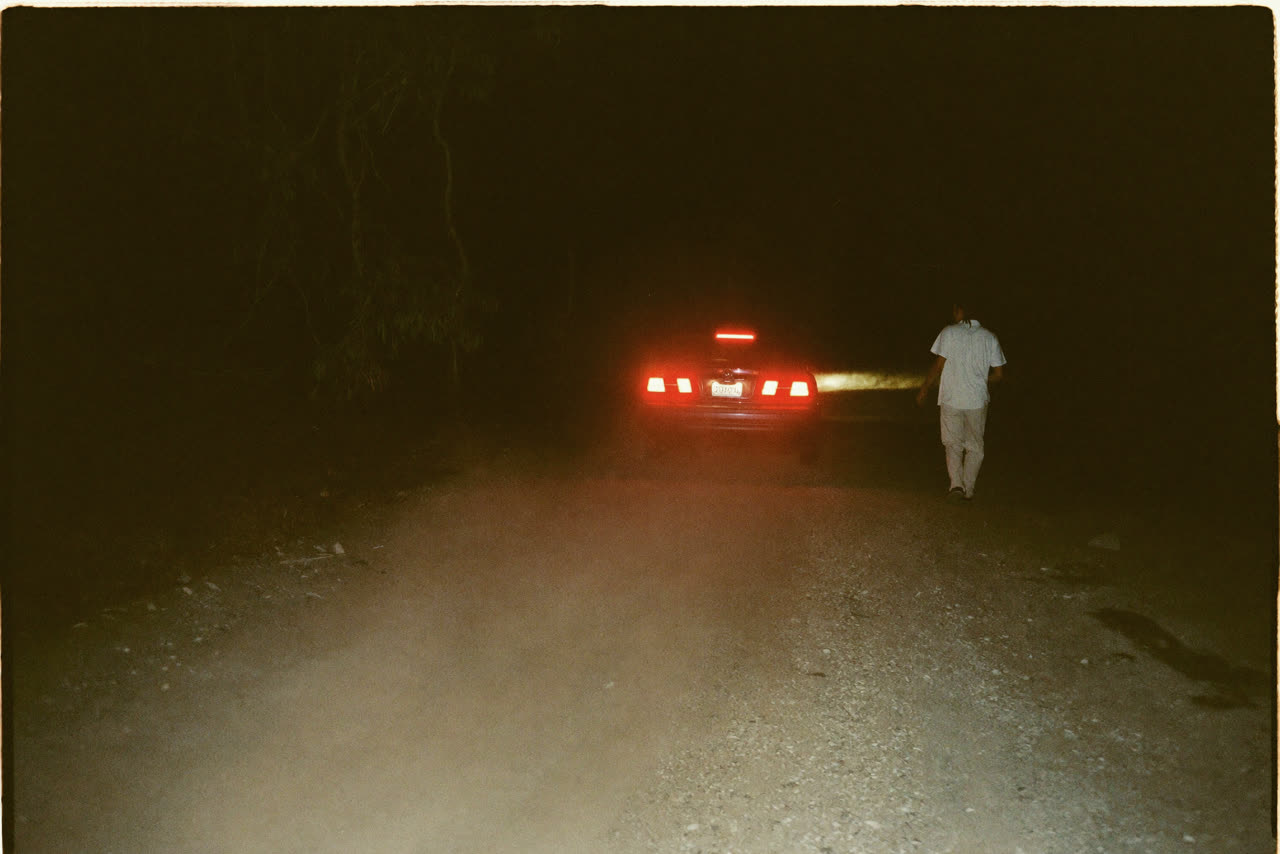 The taillights of a car going away down a dark gravel drive.